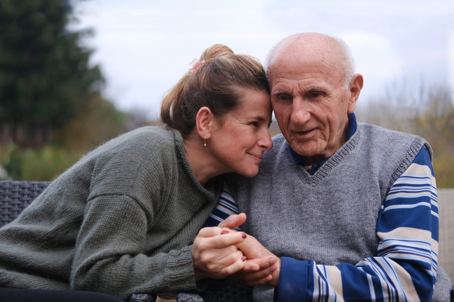 Elderly man sitting whilst his daughter comforts him