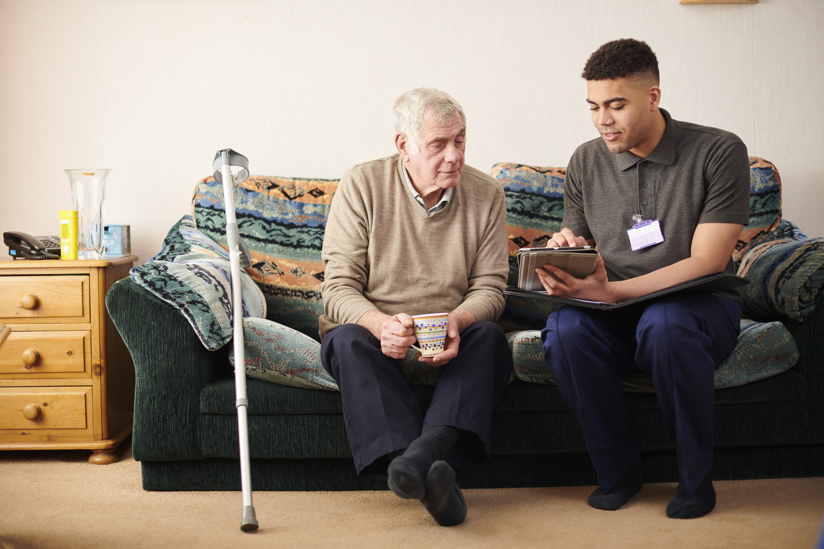 Allied health professional speaking with elderly patient whilst sitting on a green couch