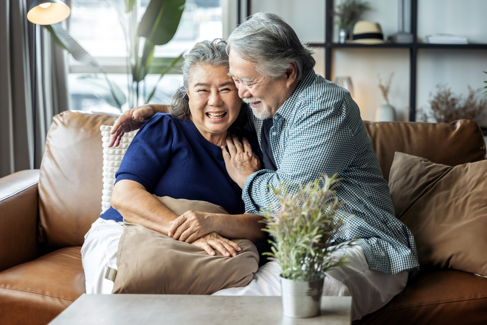 Elderly Asian couple sitting on a couch smiling at each other