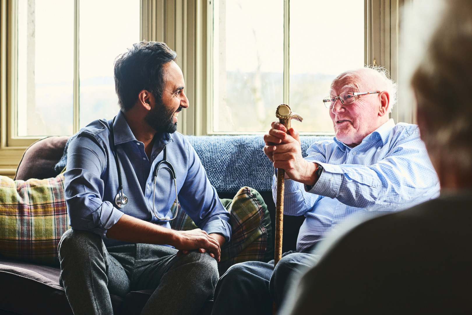 Allied health professional speaking with elderly patient whilst sitting on a green couch