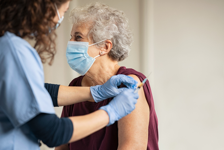 An elderly woman receiving a vaccination from a nurse