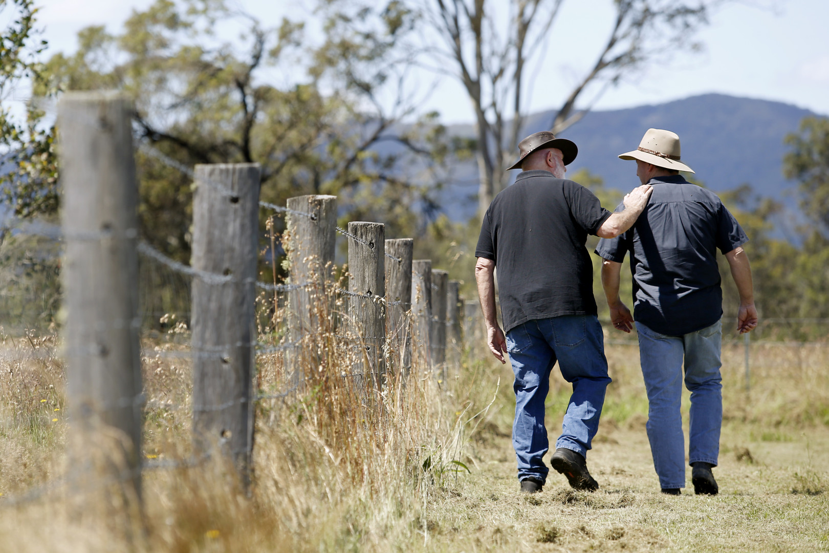 Two farmers walking along a farm fence talking