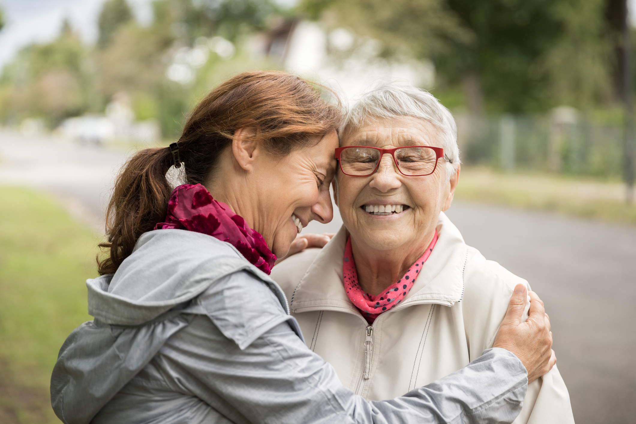 An elderly woman and her daughter smiling at the camera whilst hugging
