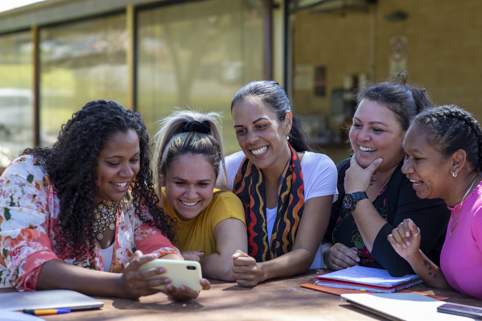 Aboriginal women smiling with each other whilst looking at a phone.